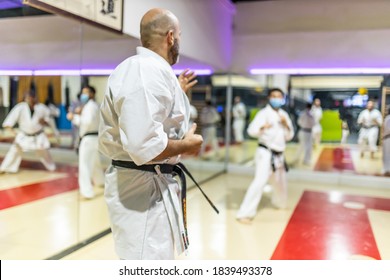 Young Adult Male Training Karate In Dojo With Face Mask, In Class With More Classmates