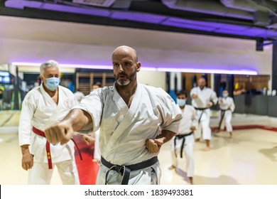 Young Adult Male Training Karate In Dojo With Face Mask, In Class With More Classmates