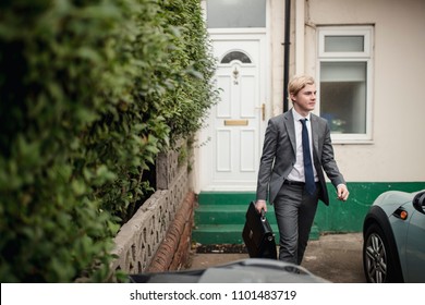 Young adult male walking you the house to go to the car to drive to work. He is dressed in a suit and tie and holding a breifcase.