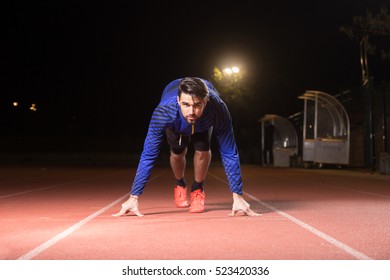 Young Adult Man, Athlete, Runner, Sprinter, Start Position, Running Track. Dark Night Time.