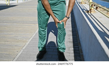 A young adult man in casual attire standing on a sunny urban boardwalk touching his knee. - Powered by Shutterstock