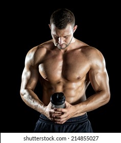 Young Adult Man Drinking Protein Shake In Gym. Black Background.