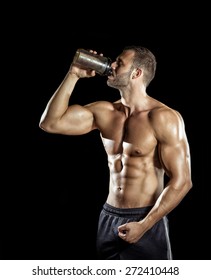 Young Adult Man Drinking Protein Shake In Gym. Black Background.