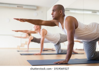 Young Adult Man Exercising Yoga With Group Of Sporty People In Studio