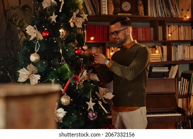 Young Adult Man With Eyeglasses Decorating Christmas Tree At Home