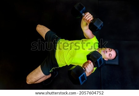 young adult man fitness training indoor in gym isolated on black backgound doing weight lifting. directly above view of person making exercises. fit, train, health and lifestyle. dark editing concept