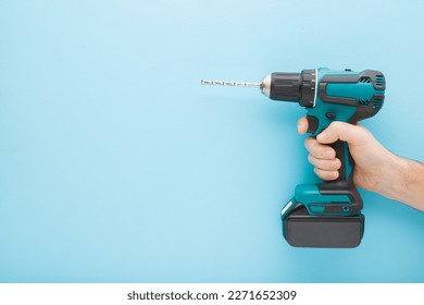 Young adult man hand holding and showing dark black green professional battery driver drill on light blue wall background. Pastel color. Closeup. Tool for repair work. Side view. Empty place for text. - Powered by Shutterstock