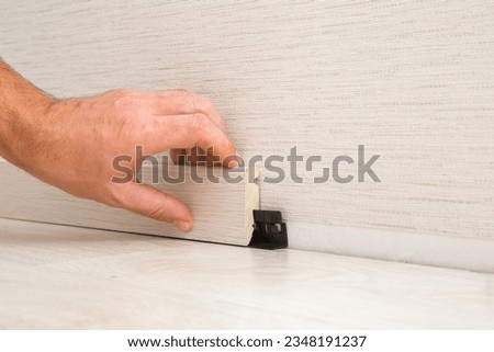 Young adult man hand installing new beige baseboard on wall and laminate floor. Repair work of home. Renovation process. Closeup. Side view. Imagine de stoc © 