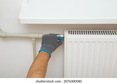 Young adult man hand in protective glove turn on or turn off valve of white radiator. Plumber connecting heat at home. Heating season. Energy efficient concept. Closeup.