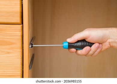 Young adult man hand using manual screwdriver and screwing screw in board of drawer for rail hinge. Assembling new wooden furniture. Closeup.