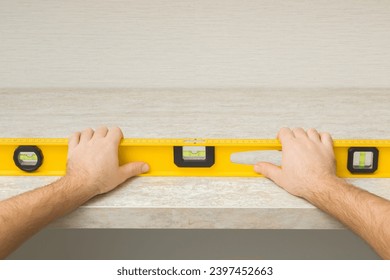 Young adult man hand using yellow spirit level and measuring horizontal surface of beige stone tabletop. Assembling new kitchen furniture. Closeup. Point of view shot. Renovation process. - Powered by Shutterstock