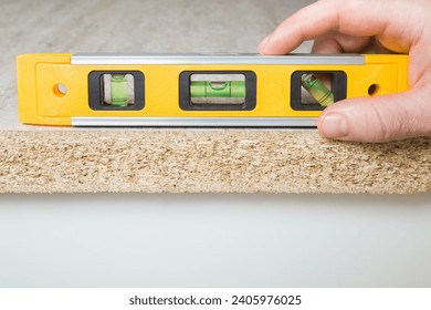 Young adult man hand using yellow spirit level and measuring horizontal surface of beige tabletop. Assembling new kitchen furniture. Closeup. Front view. Renovation process. - Powered by Shutterstock