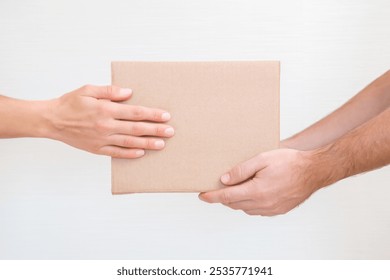 Young adult man hands holding and giving brown carton box to woman at gray wall background. Different things, goods, food or other products delivering. Closeup. Front view. - Powered by Shutterstock