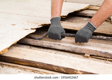 Young adult man hands in protective gloves using crowbar and breaking old wooden floor. Closeup. Preparing for repair work of home. Flooring change.