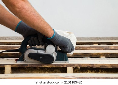 Young adult man hands in protective gloves using jointer and shaving old wooden floor planks. Closeup. Side view. Preparing for repair work of home. Flooring restoration.