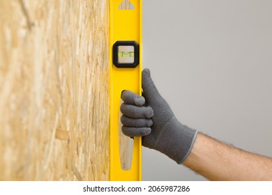 Young adult man hands using yellow spirit level and measuring vertical surface of osb board for new wall. Closeup. Preparing for repair work of home. Renovation process. - Shutterstock ID 2065987286