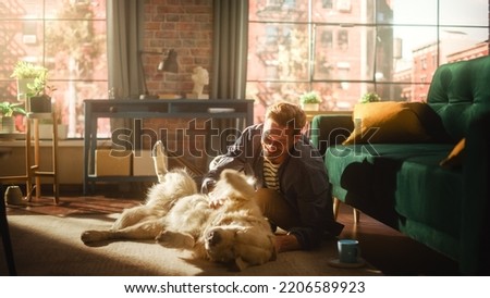 Young Adult Man Having Fun and Playing with His Golden Retriever Pet on a Living Room Floor. Attractive Dog Owner Petting, Scratching and Teasing His Canine Best Friend at Home.