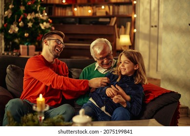 Young adult man, his father and son sitting on sofa in the living room. Father and father tickling little boy while enjoying Christmastime at home - Powered by Shutterstock