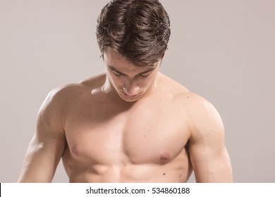 Young adult man, looking down, upper body, chest  arms, close up. Background, studio.