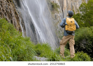 Young adult man on his back with yellow backpack in front of a waterfall taking a hiking route admiring the mountain, pure and wild nature, jungle, nature reserve, national park - Powered by Shutterstock