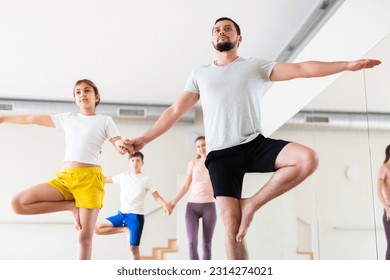 Young adult man practicing yoga in pair with teen daughter, performing double tree pose during family workout at gym