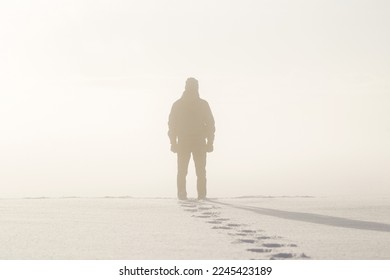 Young adult man silhouette standing in nature mist and looking far away. Thinking about life. Back view. Fresh human boots footprints in fresh deep snow. Cold snowy winter day. - Powered by Shutterstock