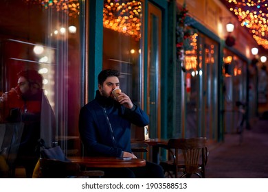 Young Adult Man Sitting Alone In Urban Outdoor Cafe On The Night Cozy Narrow Street