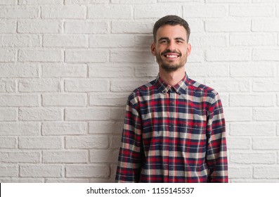 Young adult man standing over white brick wall with a happy and cool smile on face. Lucky person.