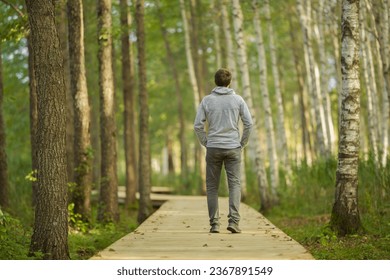 Young adult man walking on wooden trail at birch tree forest in beautiful autumn day. Spending time alone and enjoying freedom at nature. Back view. Peaceful atmosphere in nature. - Powered by Shutterstock