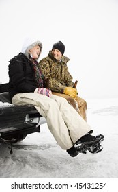 Young Adult Man And Woman Drinking Beer And Sitting On The Tailgate Of A Truck In A Winter Environment. Vertical Shot.