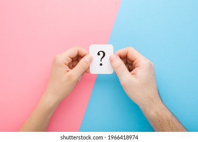 Young Adult Man And Woman Hands Together Holding White Card Of Question Mark On Light Blue Pink Table Background. Pastel Colors. Concept Of Couple Relationship Issues. Closeup. Point Of View Shot.