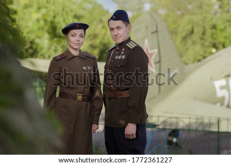 Young adult man and woman in the uniform of pilots of the Soviet Army of the period of World War II. Military uniform with shoulder straps of a major and a cap on his head. Photo in retro style.