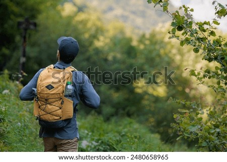 Young adult man with yellow backpack taking a hiking route in admiration of the mountain, pure and wild nature, jungle, natural reserve, national park