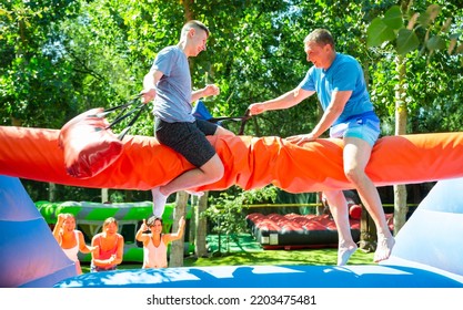 Young And Adult Men Having Pillow Fight Between Each Other In Outdoor Amusement Park During Summertime.