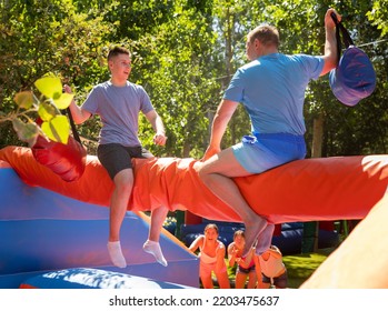 Young And Adult Men Having Pillow Fight Between Each Other In Outdoor Amusement Park During Summertime.