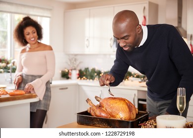 Young adult mixed race couple preparing Christmas dinner together at home, man basting roast turkey in the foreground, front view, close up - Powered by Shutterstock