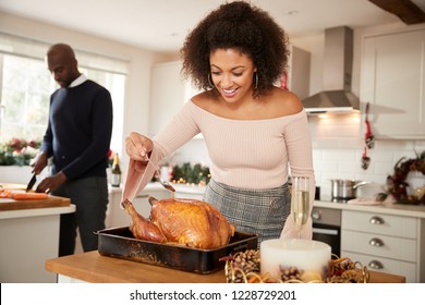 Young Adult Mixed Race Couple Preparing Christmas Dinner Together At Home, Woman Basting Roast Turkey In The Foreground, Front View, Close Up