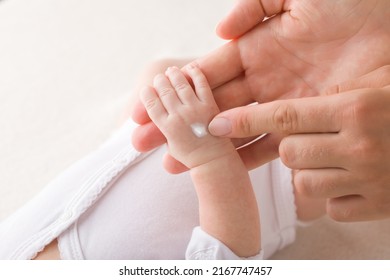 Young Adult Mother Applying White Moisturizing Cream On Newborn Hand. Care About Baby Clean And Soft Body Skin. Closeup.