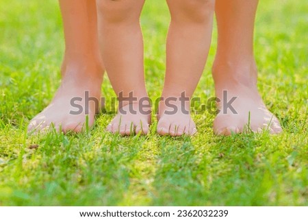 Young adult mother and baby standing together with barefoot on fresh green grass at park in beautiful warm sunny summer day. Front view. Closeup.