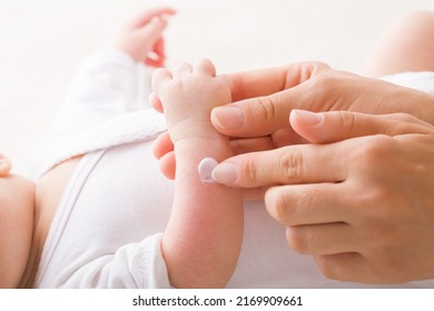 Young adult mother finger applying white medical ointment on newborn arm. Red rash on skin. Allergy from milk formula or mother milk. Care about baby body. Closeup. Side view. - Shutterstock ID 2169909661