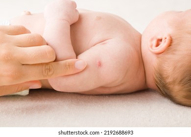 Young Adult Mother Finger Pointing To Red Point After Tuberculosis Vaccine On Newborn Shoulder Skin. Baby Healthcare Concept. Closeup.