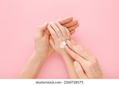 Young adult mother fingers applying white moisturizing cream on little girl hand on light pink table background. Pastel color. Care about baby clean and soft body skin. Closeup. - Powered by Shutterstock