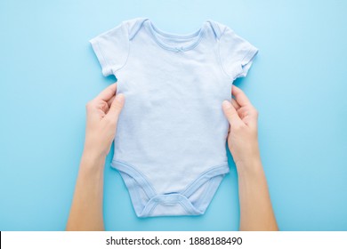 Young adult mother hands holding new baby boy bodysuit on light blue table background. Pastel color. Closeup. Point of view shot. Empty place for text or logo on apparel.