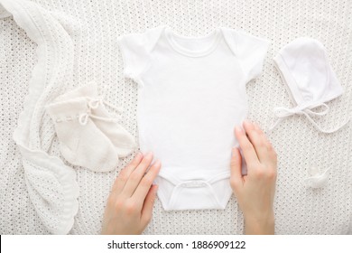 Young adult mother hands touching newborn bodysuit on light white blanket background. Closeup. Point of view shot. Preparing baby clothes.
