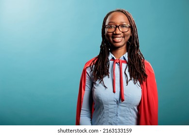 Young adult optimistic and strong superhero woman wearing hero cloak. Happy smiling heartily mighty and brave justice defender standing on blue background while looking at camera. - Shutterstock ID 2163133159
