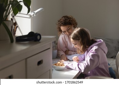 Young Adult Parent Mother Or Tutor Studying With Teen Daughter At Home Together. Mom Helping School Child Girl With Homework Reading Book Explaining Education Assignment Sitting At Table In Cozy Room.