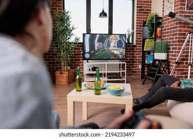 Young Adult Playing Shooting Video Games Strategy At Home, Having Fun With Friends At House Party. Gaming Competition At Gathering With Bottles Of Beer And Snacks, Entertainment.