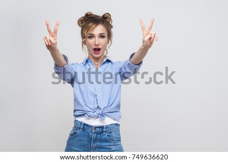 Young adult pretty beautiful blonde woman with blue dress and head band showing peace sign. Isolated studio shot on gray background. Studio shot, gray wall