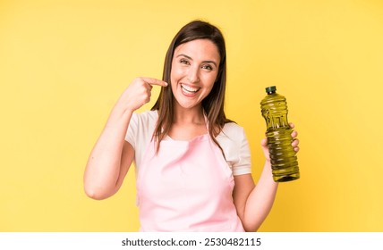 Mujer bonita joven adulta sonriendo con confianza que señala a su propia sonrisa ancha. chef casero con aceite de oliva