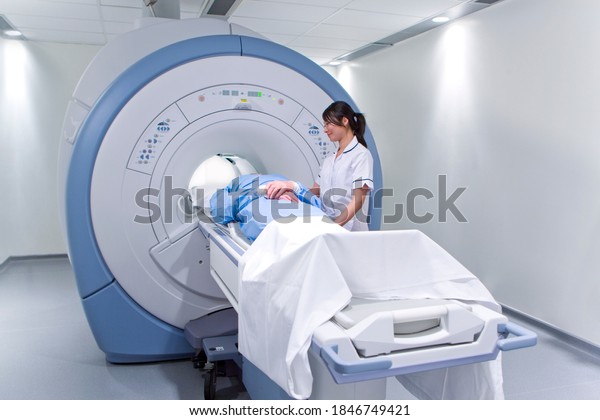 A young adult radiologist\
wearing a lab coat helps a patient with MRI scanning machine in a\
clinic